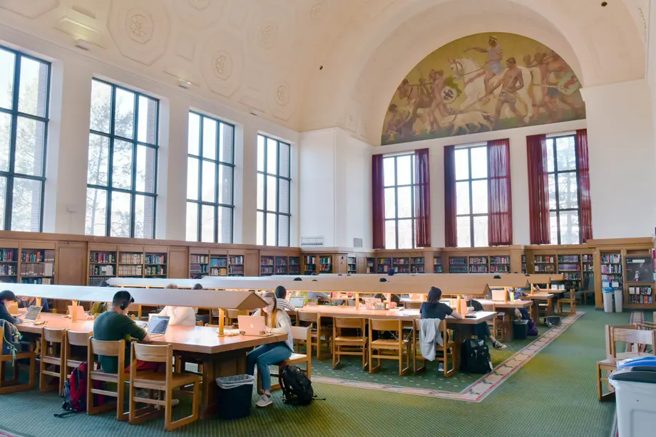 View of the Reference Reading Room with students studying at tables and the mural in the distance.