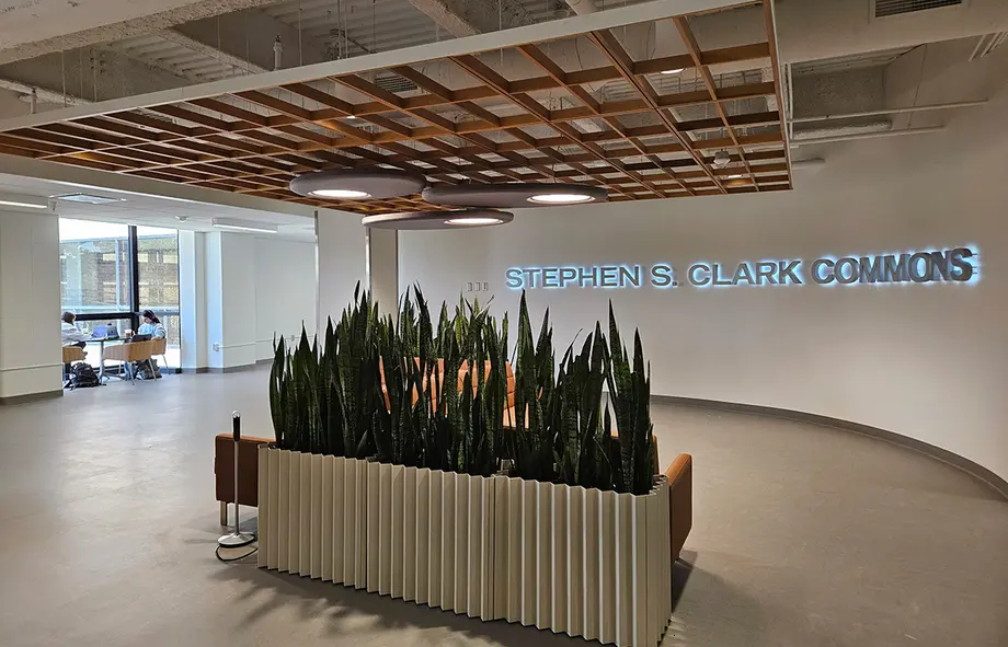 View from Clark Commons to the connector with orange couches and plants in an airy seating area and students studying in the backround.