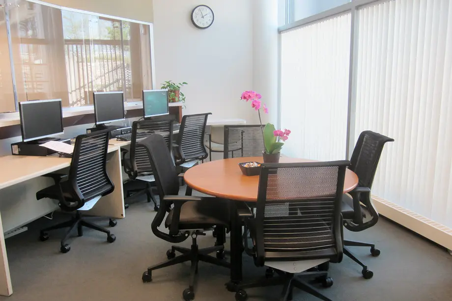 Light filled room with a round table and chairs and a few computers along the perimeter.